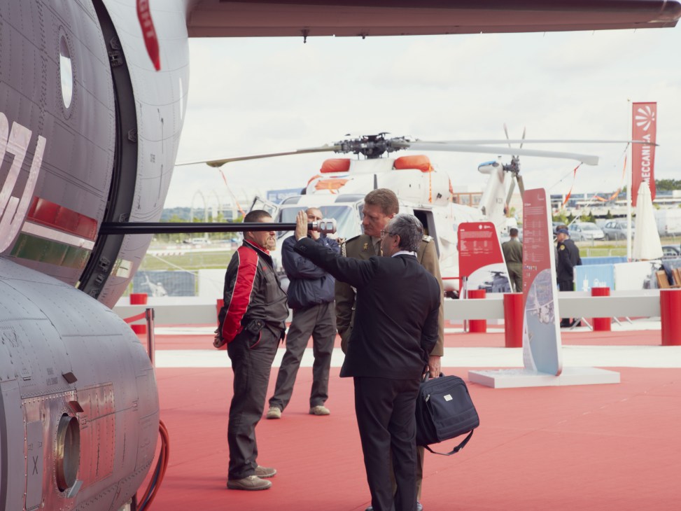 Delegates viewing aircraft at Farnborough International Air Show with helicopters in background.