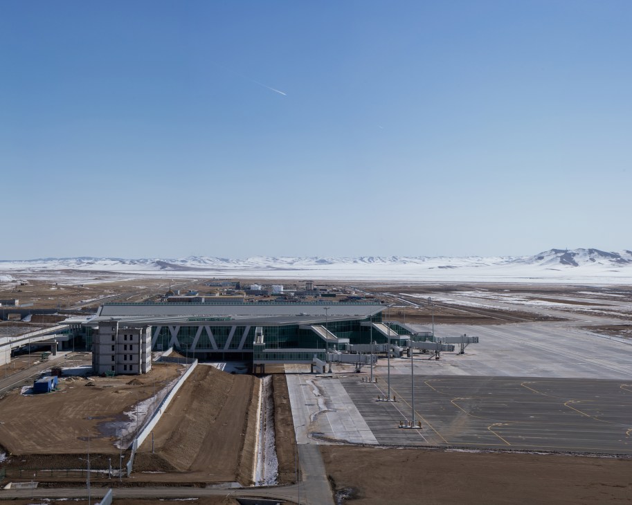 The new Chinggis Khaan International Airport terminal building under construction in a snowy Mongolian valley landscape.