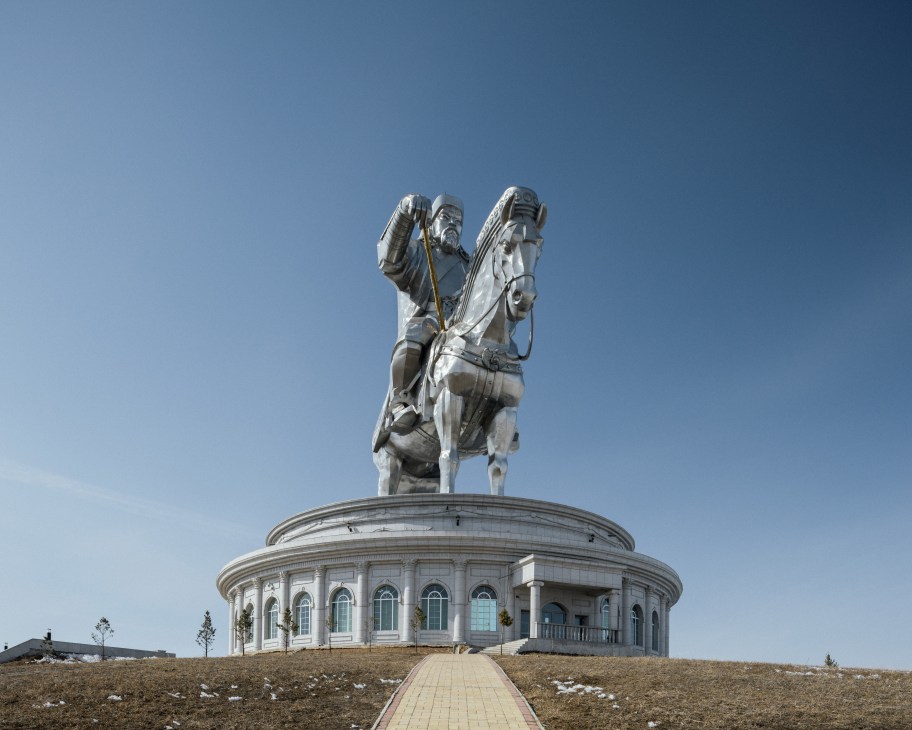 Equestrian statue of Genghis Khan on horseback atop a circular white building against a clear blue sky.