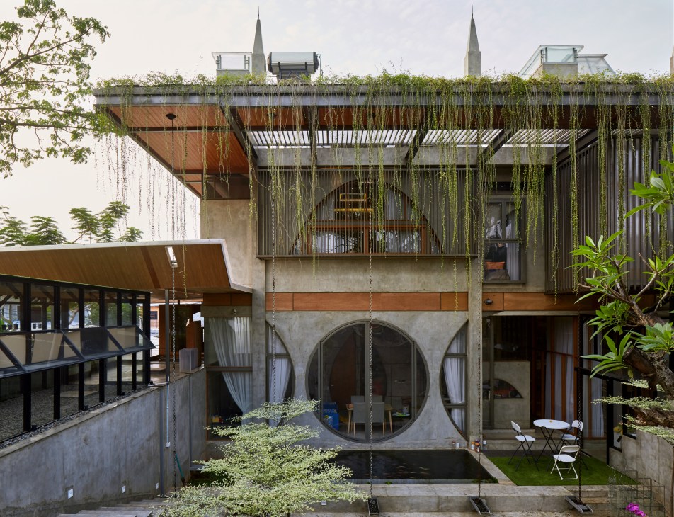 Modern concrete building with circular window, green roof garden, and tropical plants in Jakarta