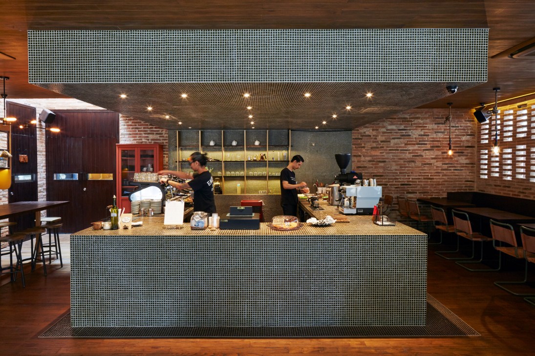 Modern coffee shop interior with mosaic tile counter, brick walls, and two baristas working behind espresso machines