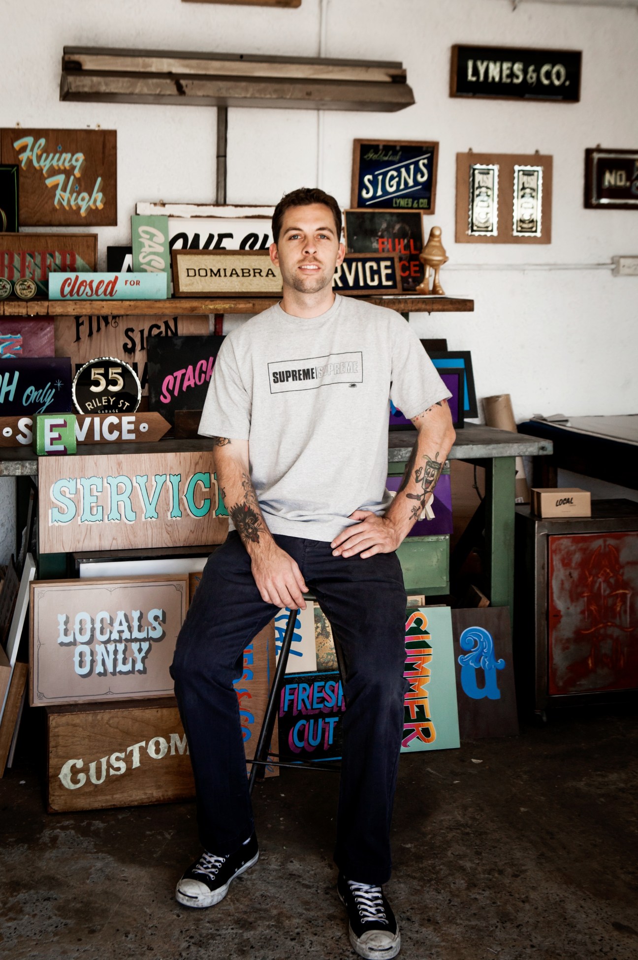 Will Lynes stands in his Sydney workshop surrounded by vintage hand-painted signs and lettering samples.