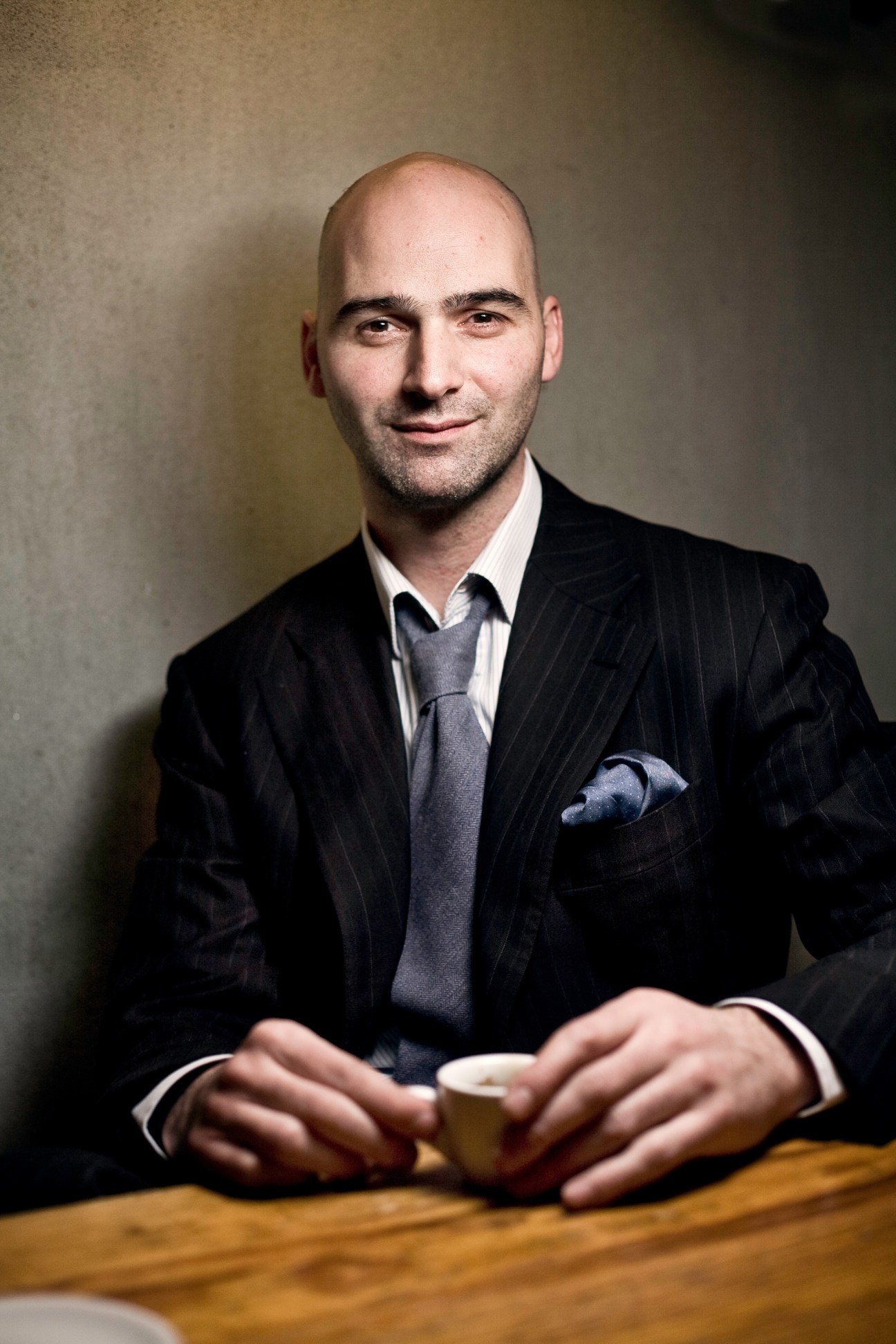 Lewis Cutillo, co-founder of Bontoni, in formal navy pinstripe suit and tie holding a coffee cup.