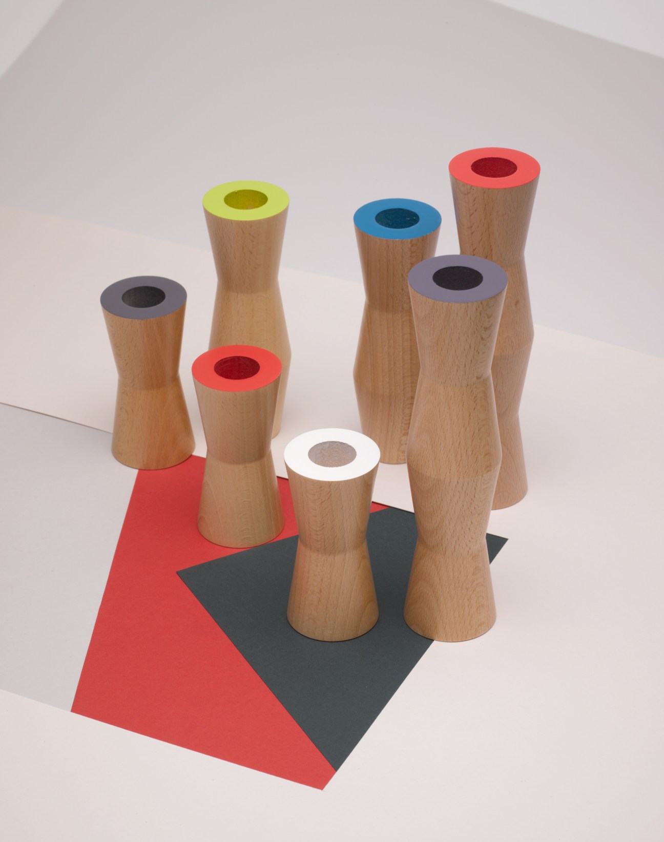 Avva Trio candlesticks in beech wood with colored collars arranged on a geometric red and black base.