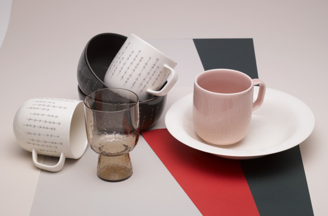 Iittala Sarjon porcelain cups and glassware with engraved arrow patterns on a geometric surface.