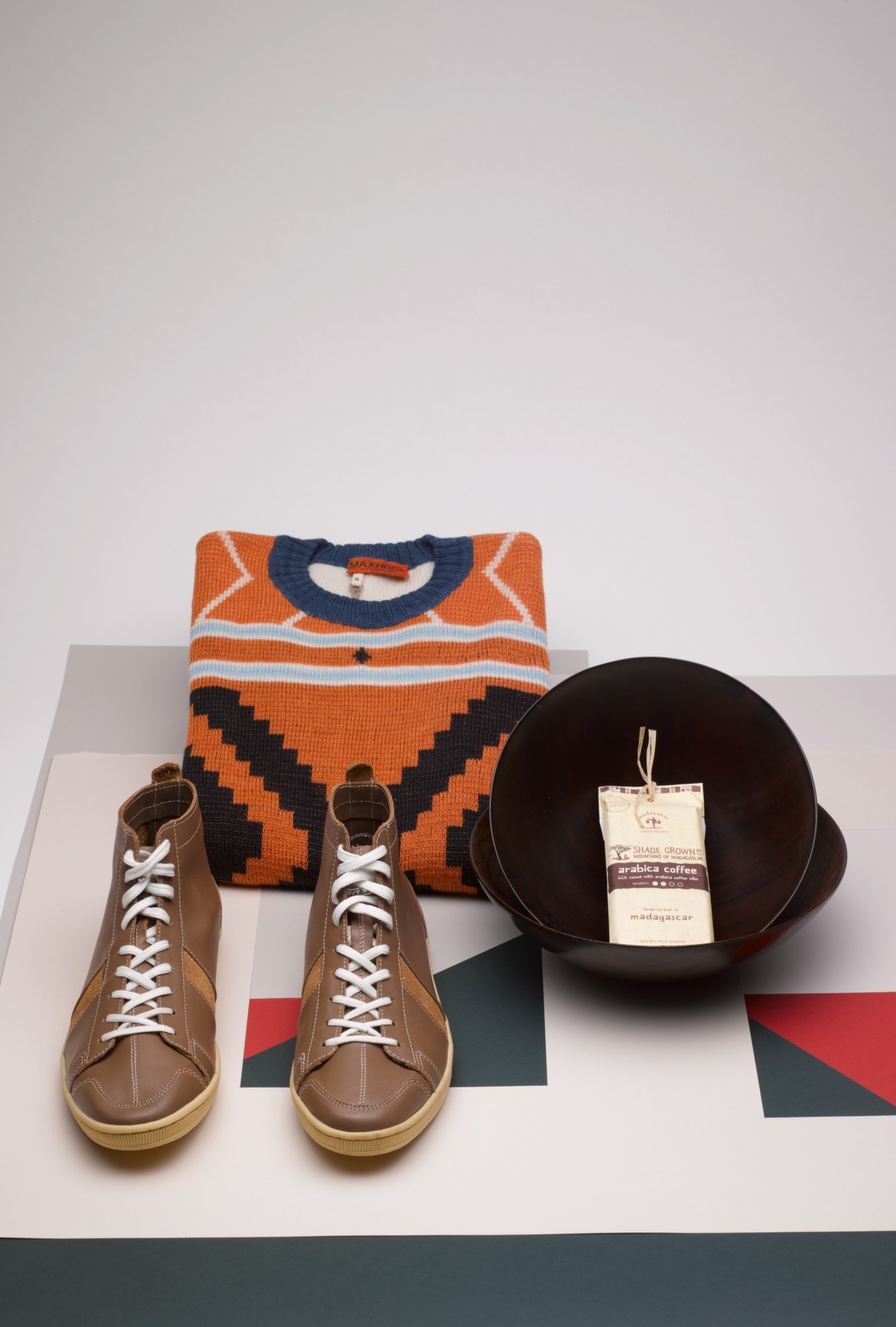 Orange and navy geometric sweater, tan lace-up boots, and black bowl with coffee tag displayed together.