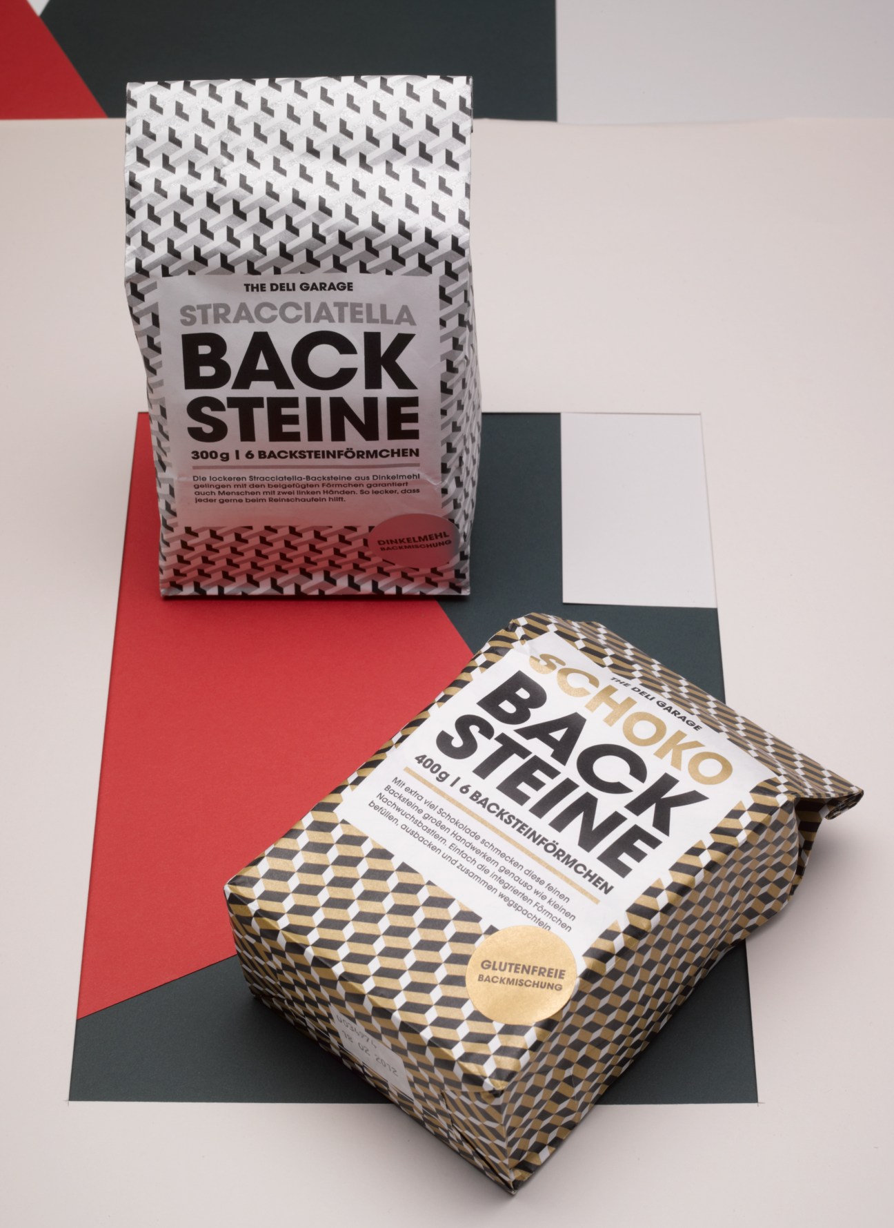 Two Backsteine cake mix packages with geometric patterned paper bags in white and gold/black designs