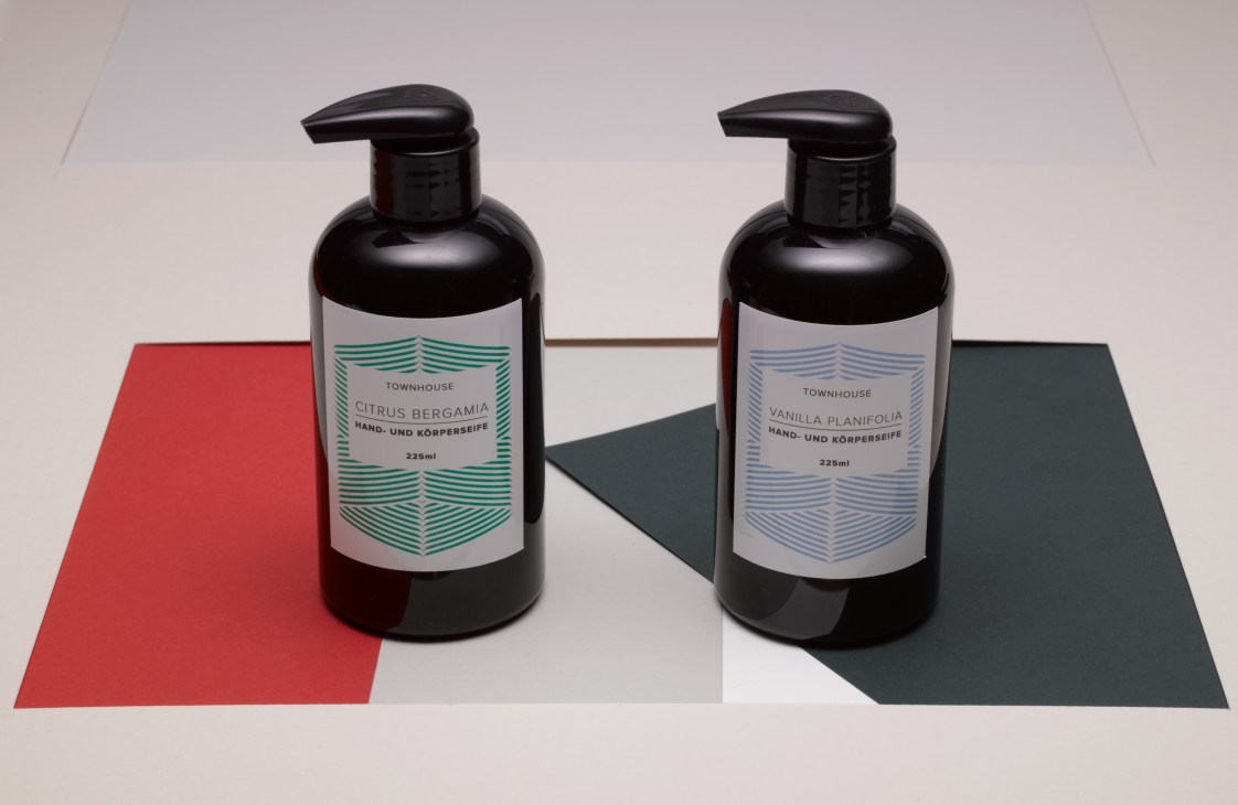 Two black pump bottles of Townhouse handmade soaps with green and blue labels on a geometric colored background.