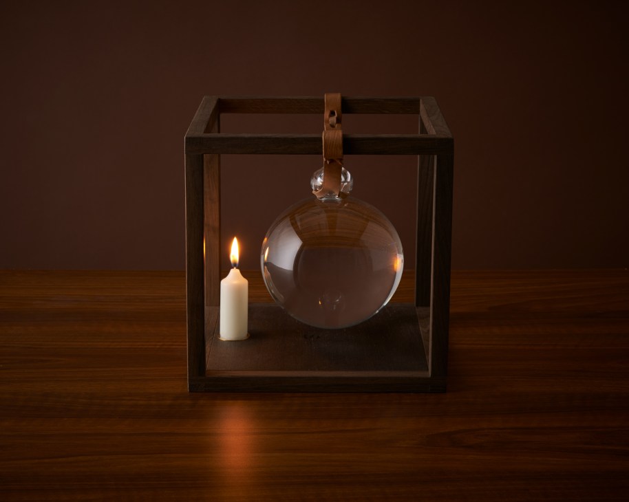 Schusterkugel lighting fixture with wooden frame, leather straps, and hand-blown glass globe illuminated by candlelight.