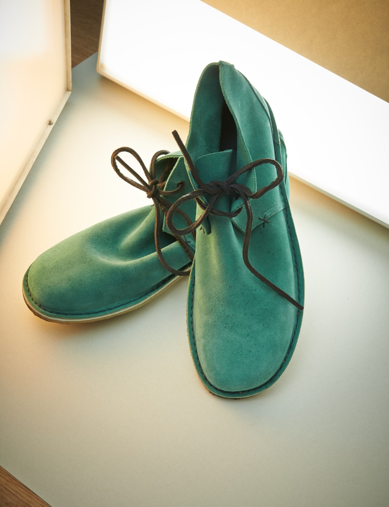 Pair of green suede desert boots with brown laces displayed on a light surface.
