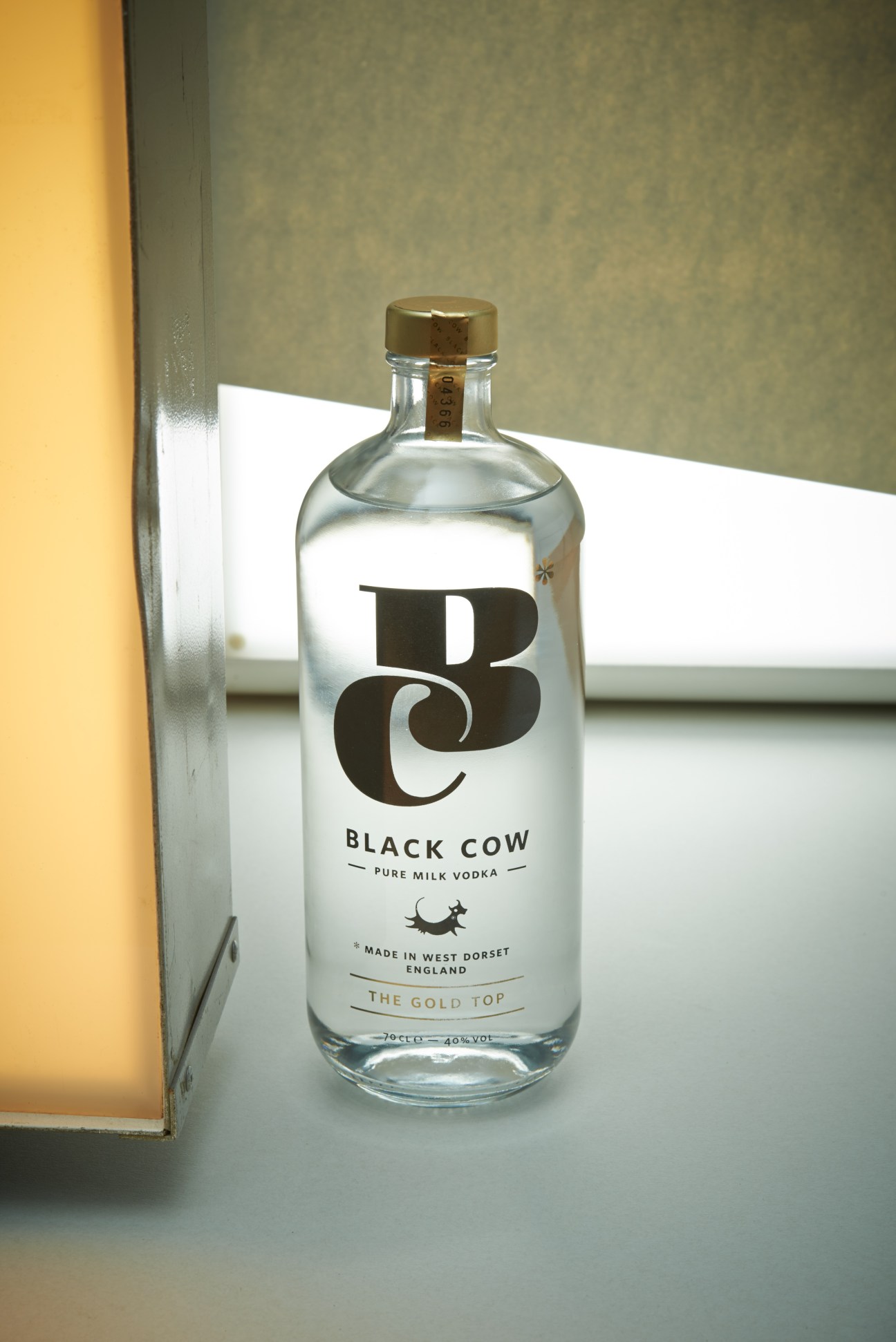 Black Cow pure milk vodka bottle with gold top and milkman-style design on white surface.