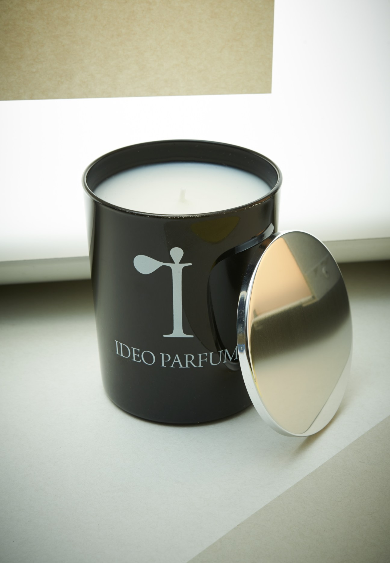 Ideo Parfums candle in black cylindrical container with metallic lid on white surface.