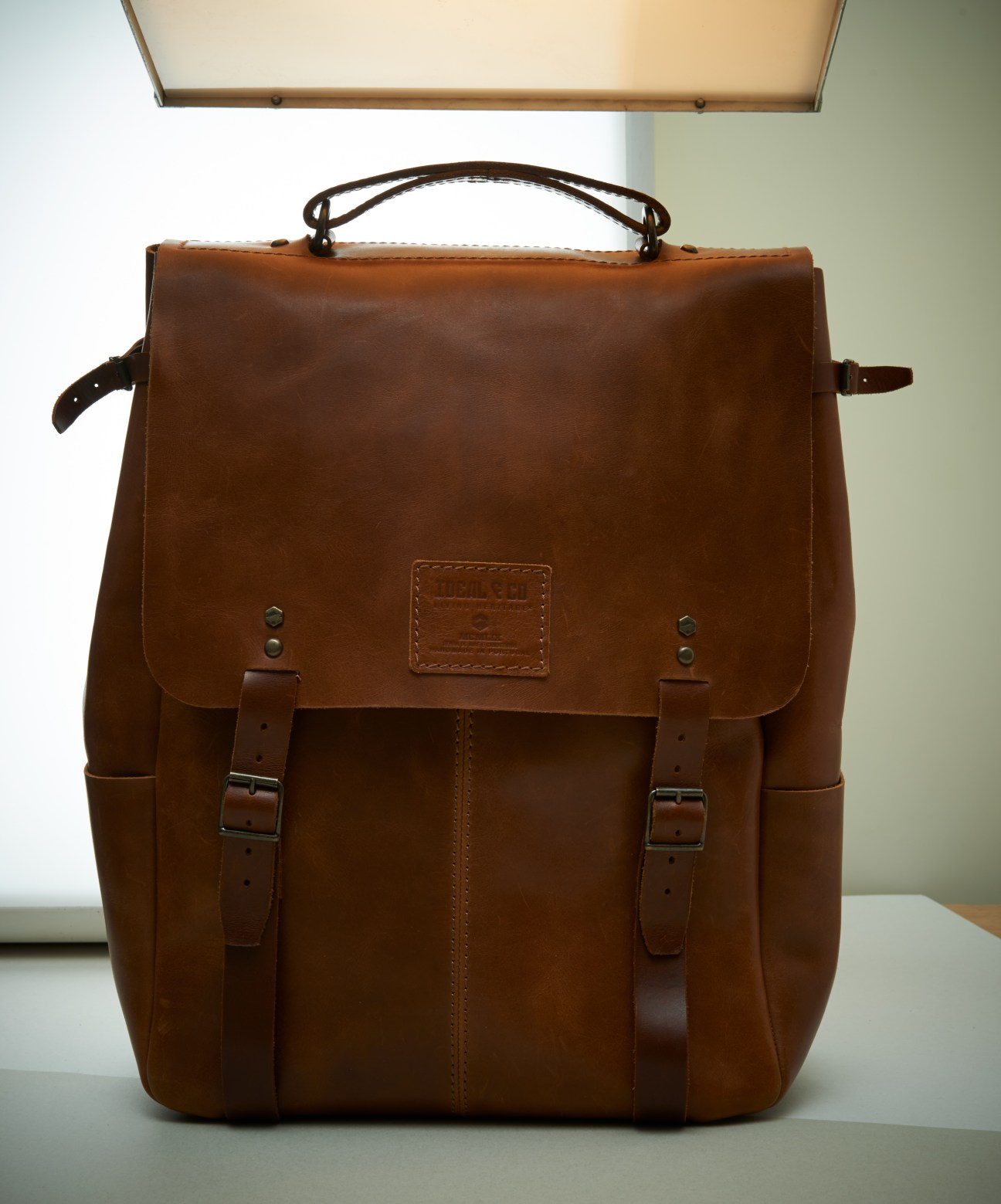 Brown leather backpack with shoulder straps and metal buckles on a white surface.