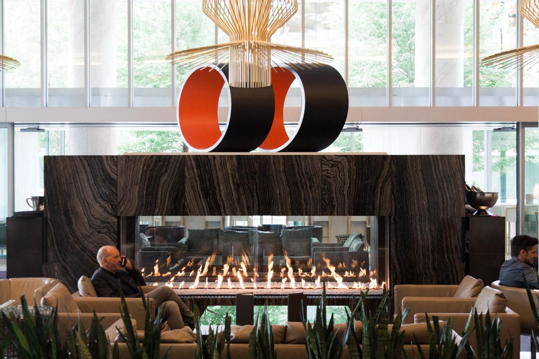 Modern lobby lounge with geometric red and black sculpture, fireplace, seating, and large windows overlooking greenery.