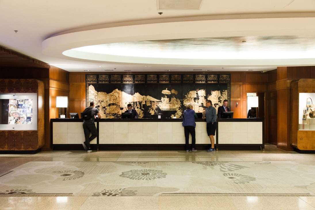 Four Seasons hotel lobby with reception desk, ornate Asian-inspired artwork, and warm wood paneling.