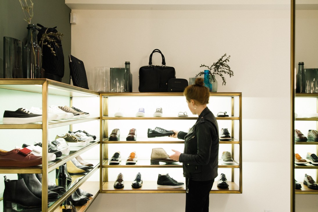 Customer browsing illuminated shelves of shoes and accessories at Want Apothecary boutique.