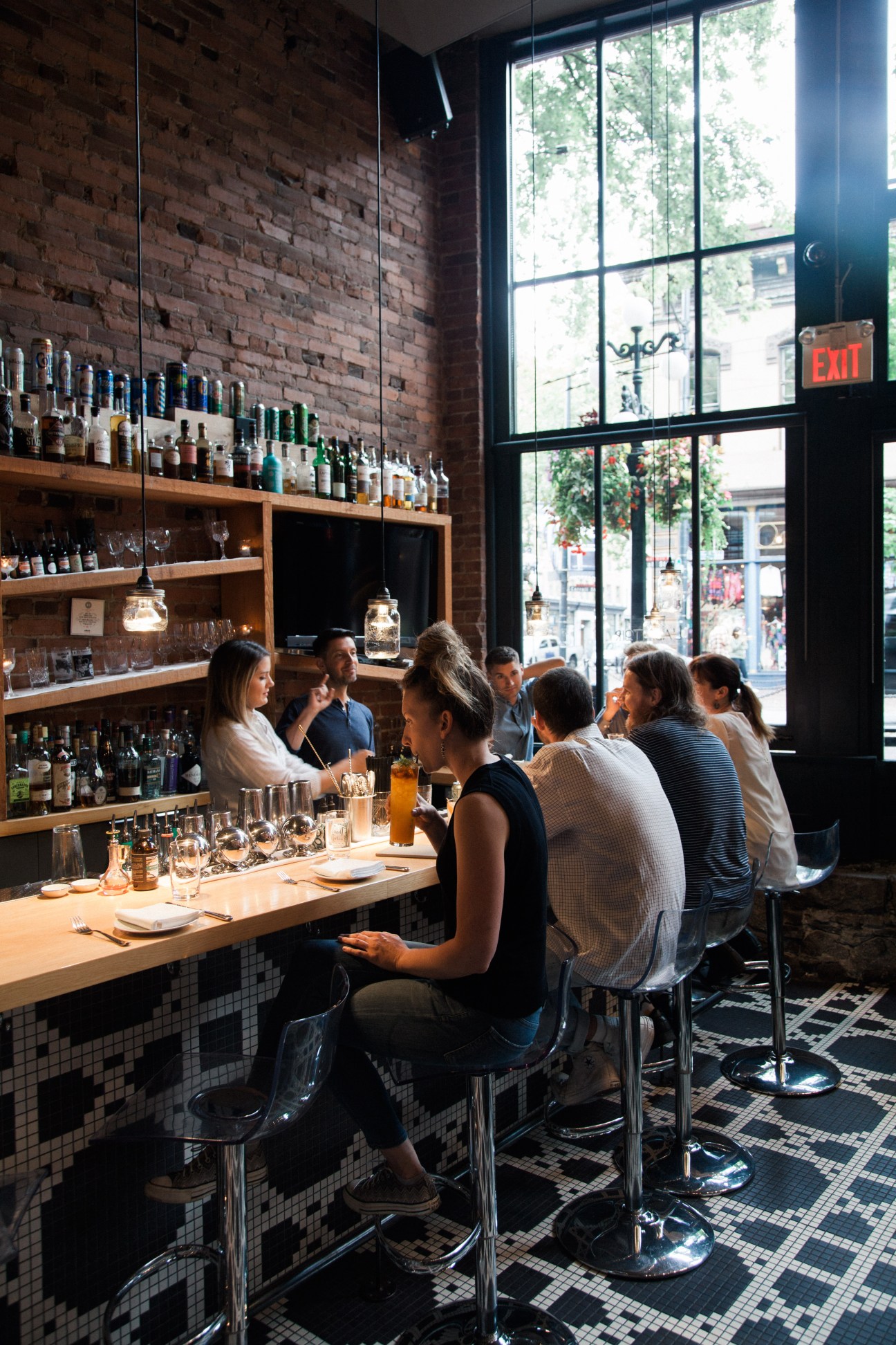 Diners seated at a bar counter at L'abattoir restaurant with exposed brick walls and shelves of spirits behind.