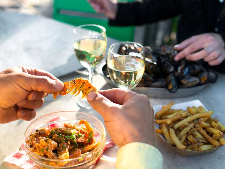 Hands holding seafood and wine glasses at an outdoor waterside meal in Bordeaux.