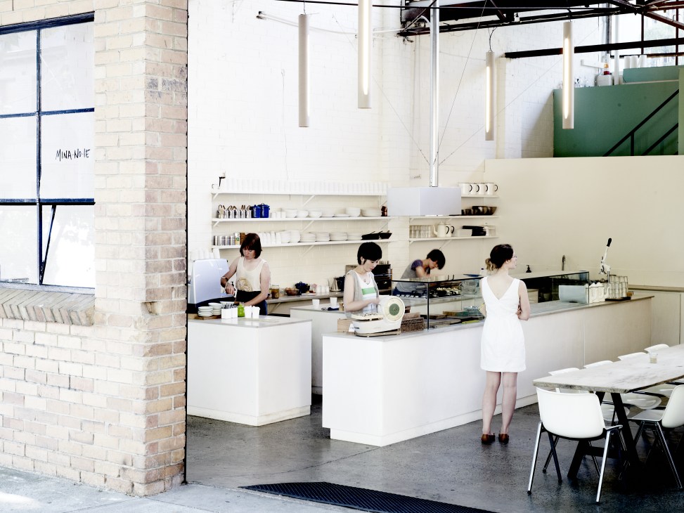 Interior of Mina-no-ie café with staff behind white counters in a minimalist space with brick walls and pendant lighting.