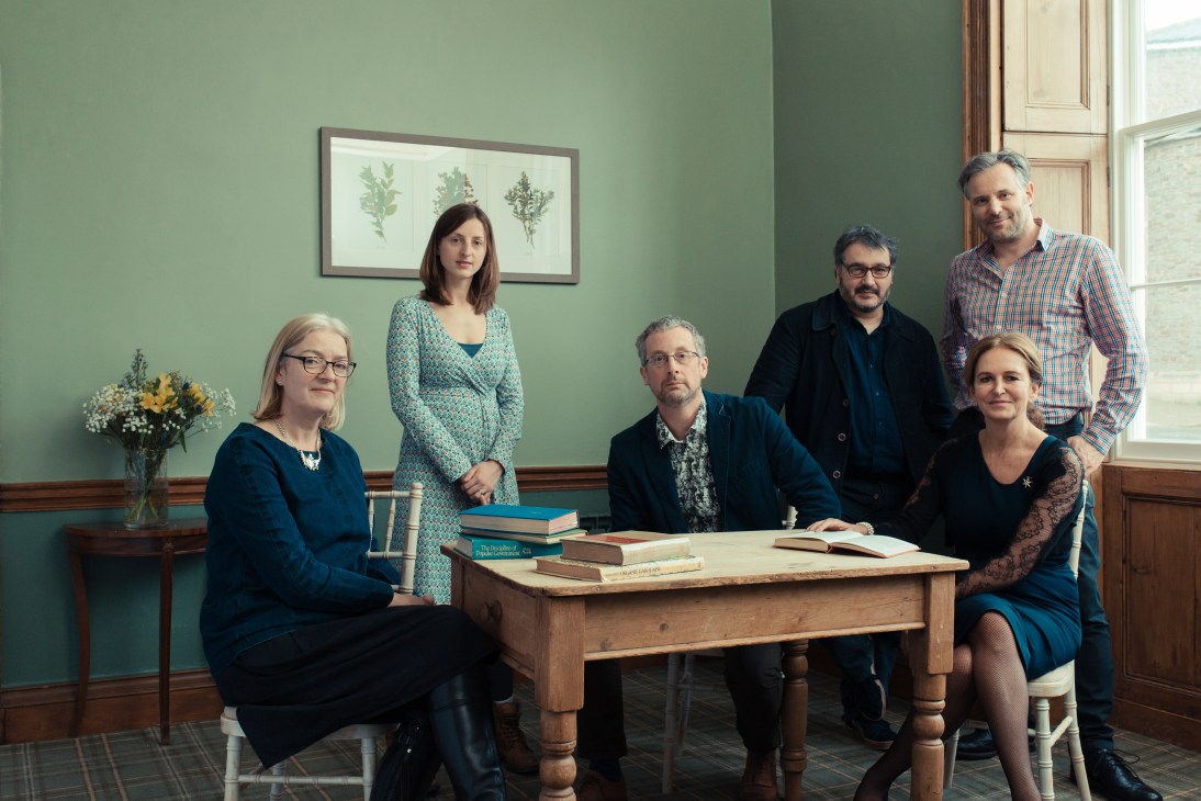 Six Hay Festival team members posed around a wooden table with books in a green-walled room.