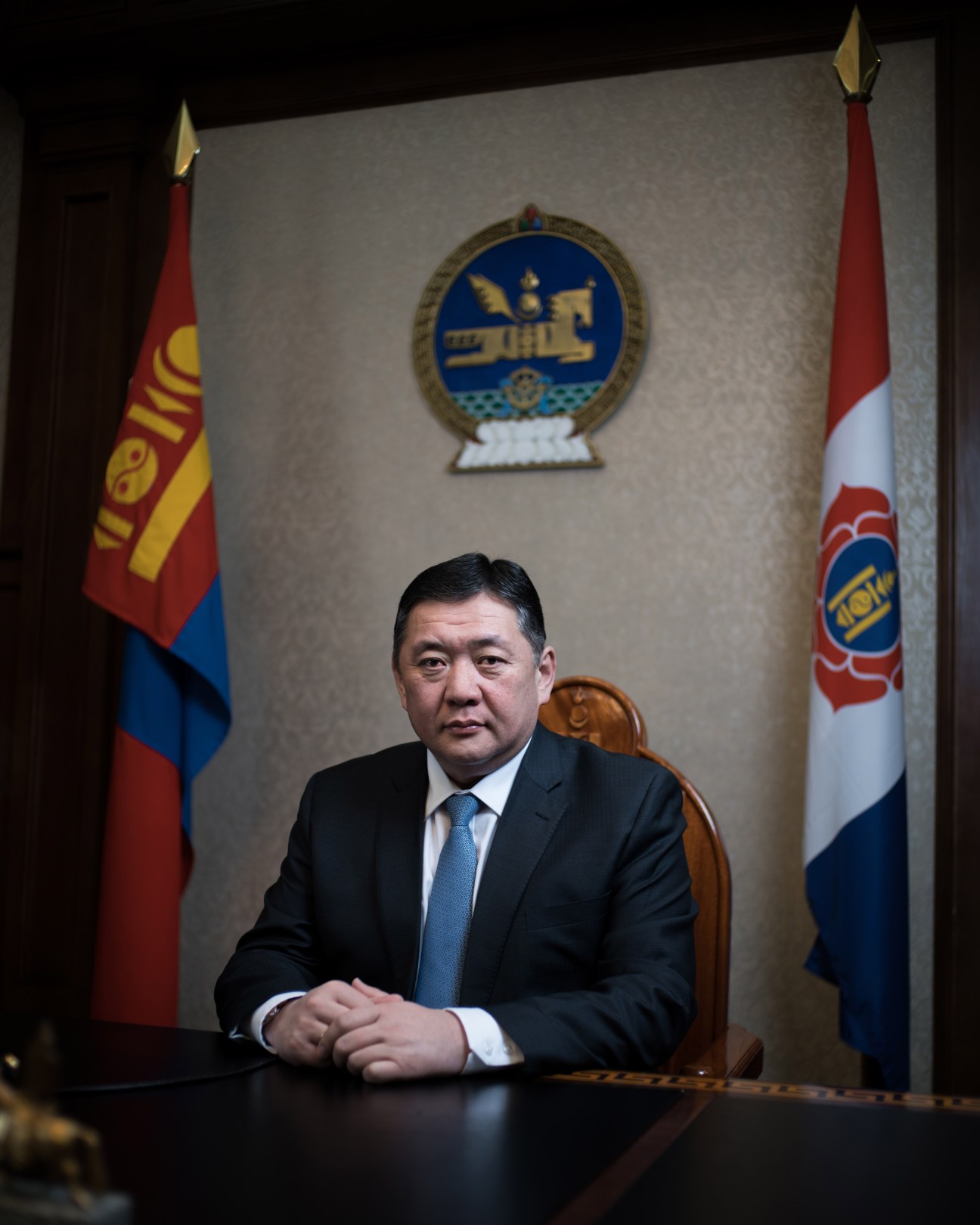 Enkhbold Miyegombiin, parliamentary speaker, seated at a desk in front of Mongolian flags and national emblem.