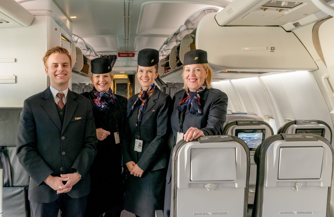 Icelandair flight attendants in uniform standing in aircraft cabin with seats visible behind them.
