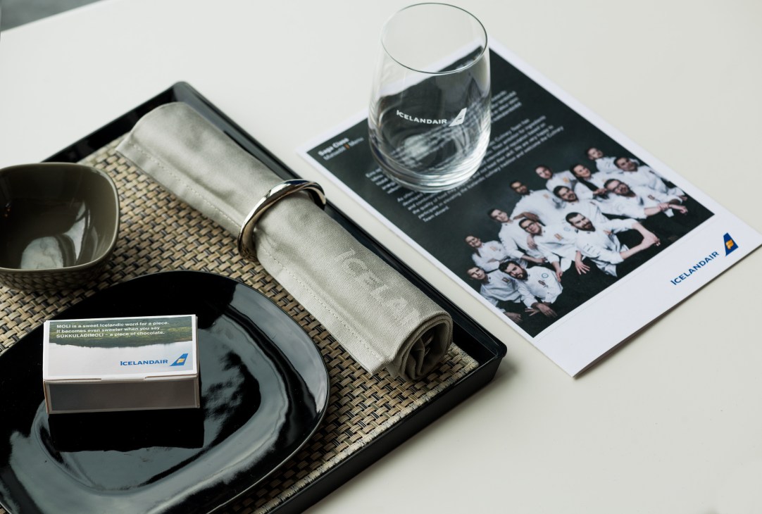Icelandair branded in-flight amenities including a glass, napkin, headrest cover and magazine on a tray.
