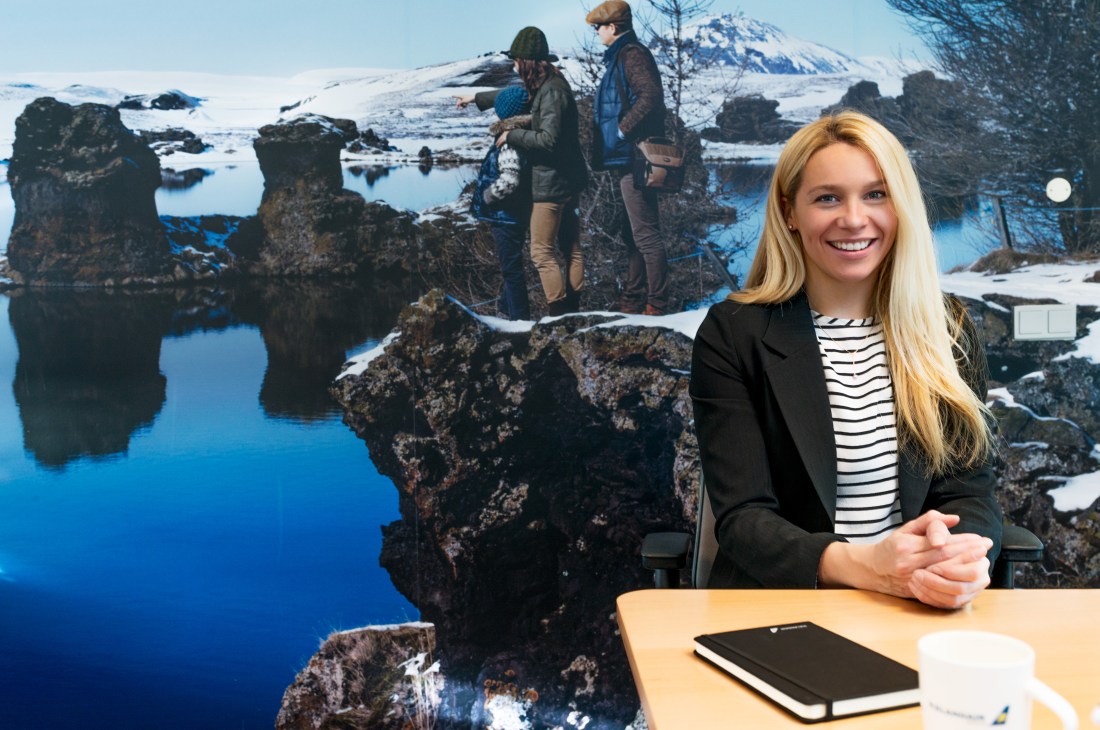 Thordis Anna Oddsdottir, director of onboard retail and service, sits at a desk with Iceland's volcanic landscape behind her.