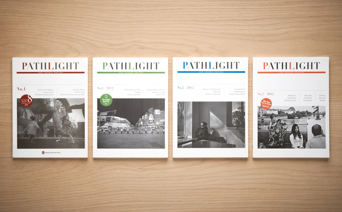Four issues of Pathlight literary magazine displayed on a wooden surface, showing covers with black and white photography.