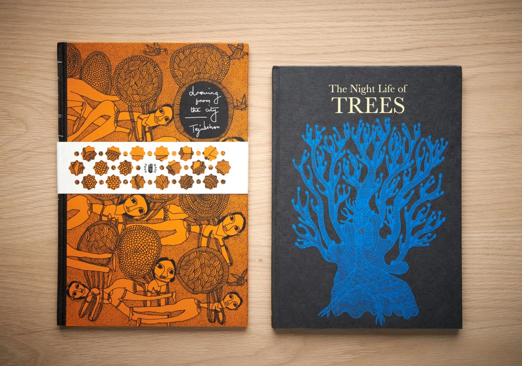 Two handmade books displayed on wooden surface: orange illustrated book titled 'Drawing from the City' and dark grey book titled 'The Night Life of Trees' with blue tree artwork.