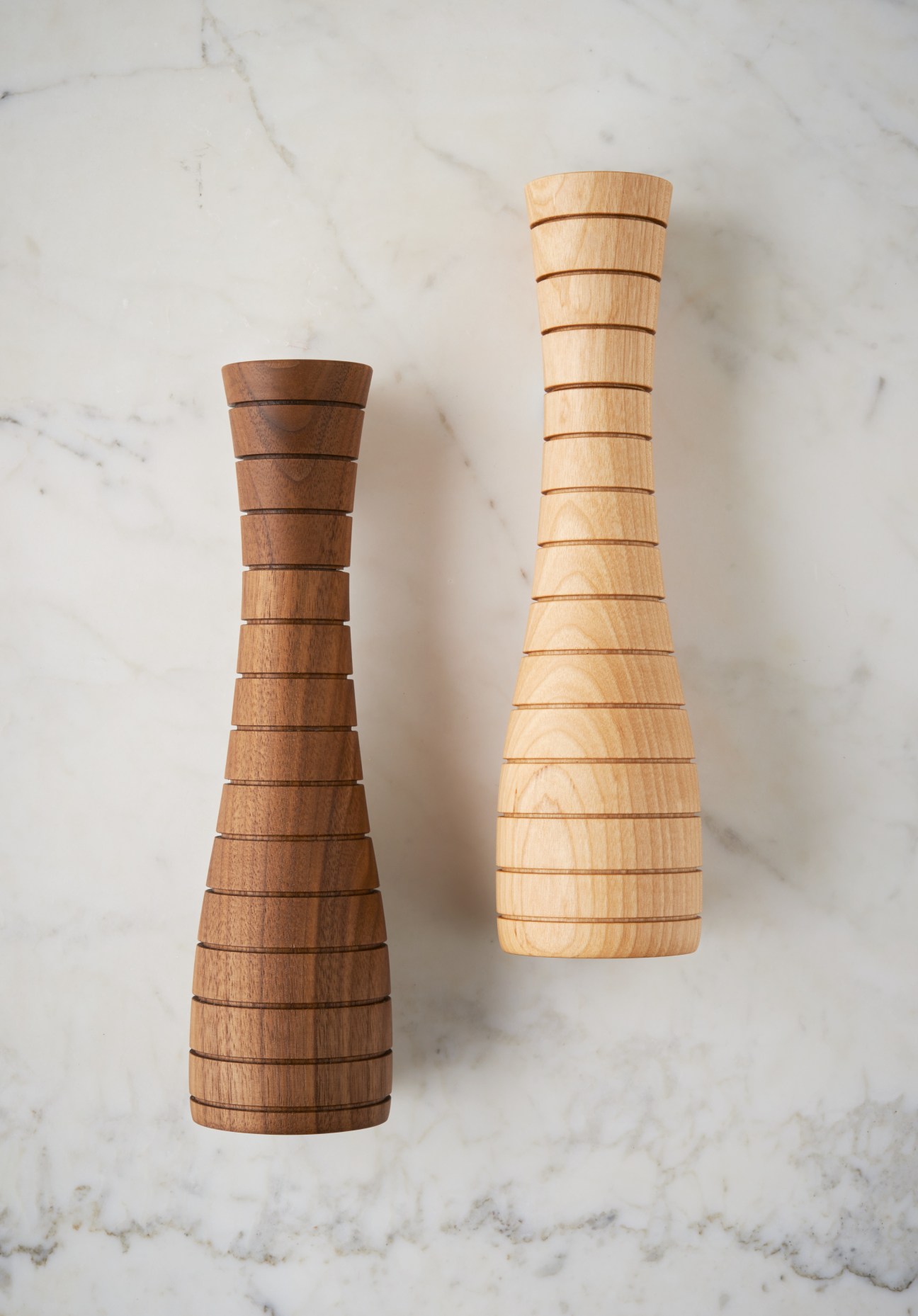 Two wooden pepper grinders in different wood tones on a marble surface.