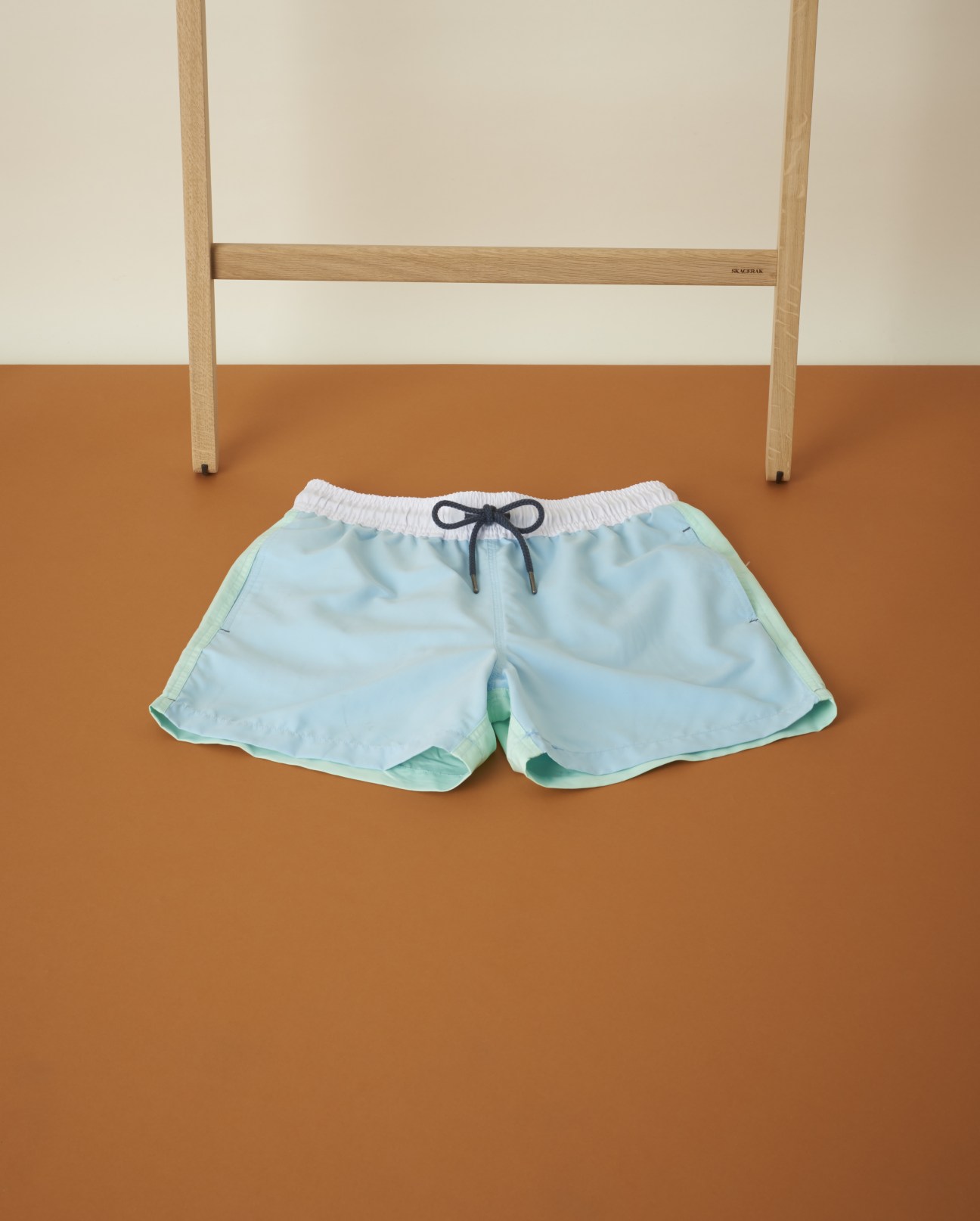 Light blue Venroy men's swimwear shorts with drawstring displayed against an orange wall.