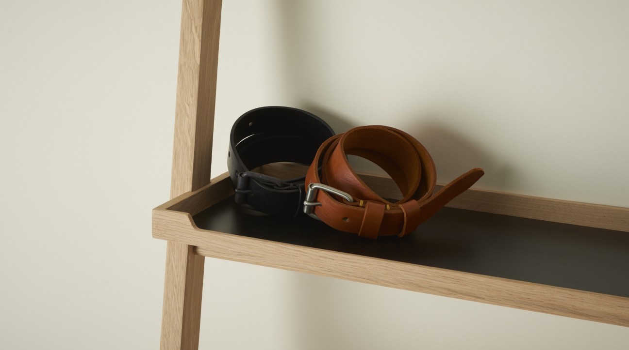 Two leather belts, one black and one cognac brown, displayed on a wooden shelf.