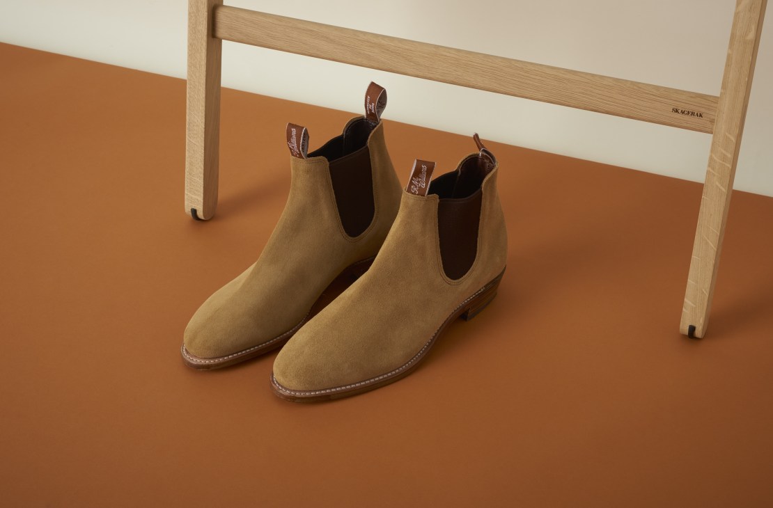 Pair of tan suede Chelsea boots with brown leather trim displayed on an orange surface.