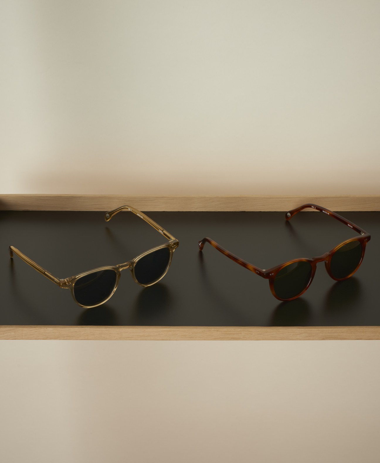 Two pairs of Pacifico Optical sunglasses displayed on a wooden shelf against a dark background.