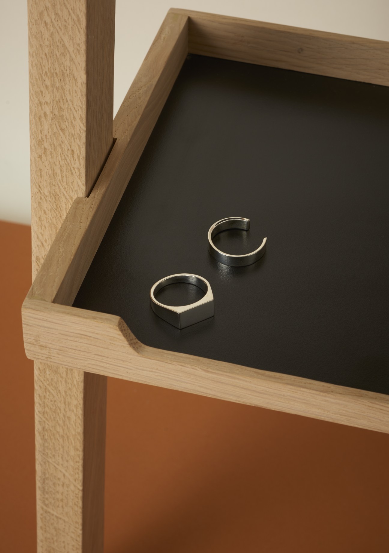 Two silver men's rings displayed on a black surface inside a wooden shelf.