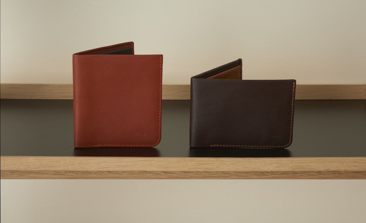 Two leather wallets in red and dark brown displayed on a wooden shelf.