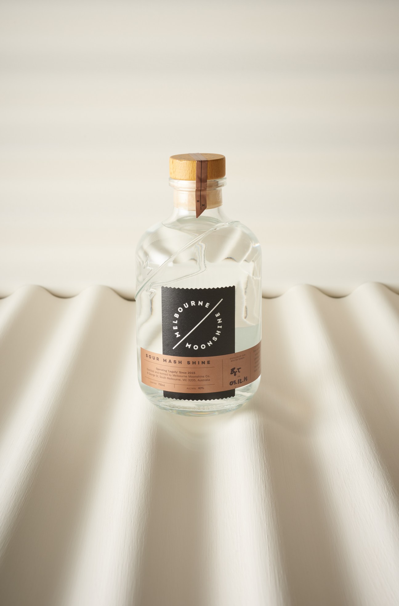 Melbourne Moonshine bottle with wooden cap and black label on white fabric background.