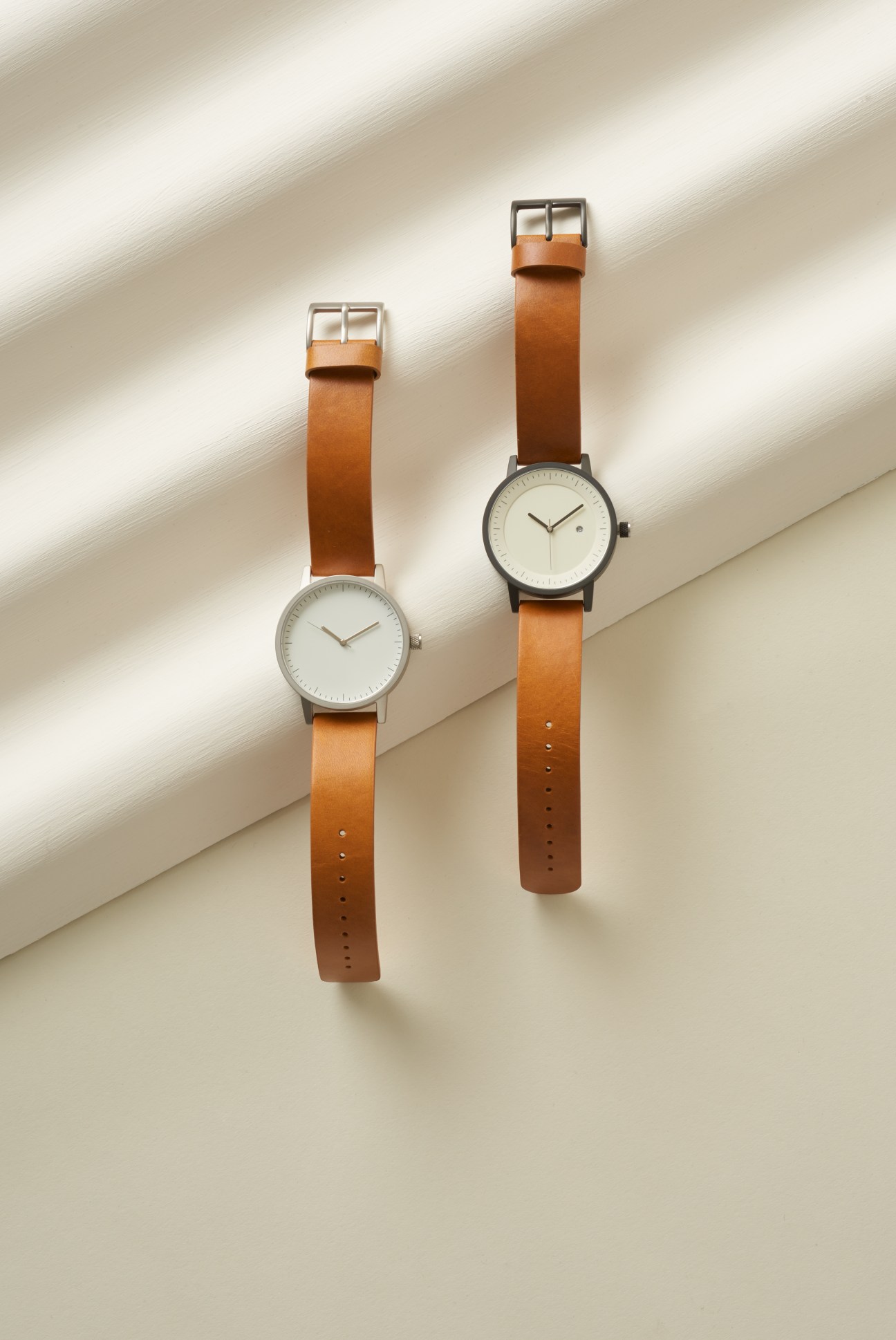 Two Simple Watch Co timepieces with cream faces and vegetable-tanned leather straps on a neutral surface.