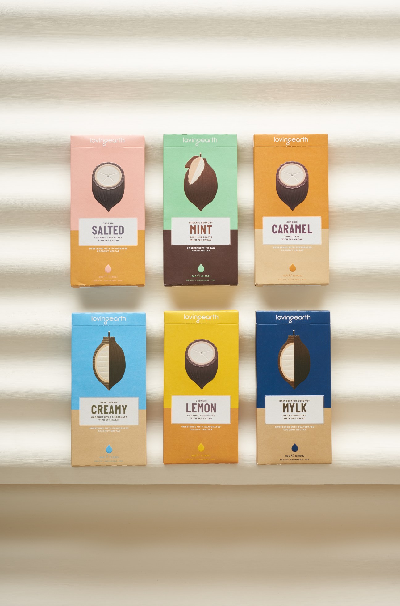 Six colorful Loving Earth chocolate bar packages with illustrated designs displayed against a striped background.