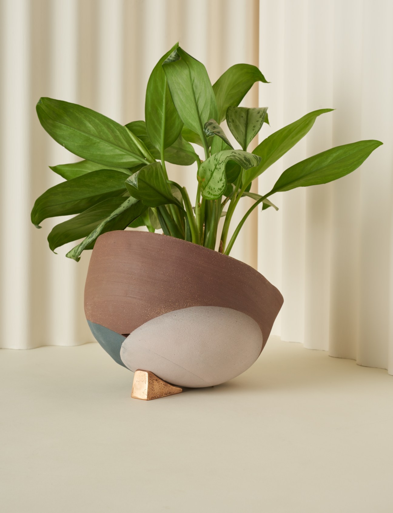 Tilted terracotta planter with white base and copper water-wicking stand holding a potted green plant.