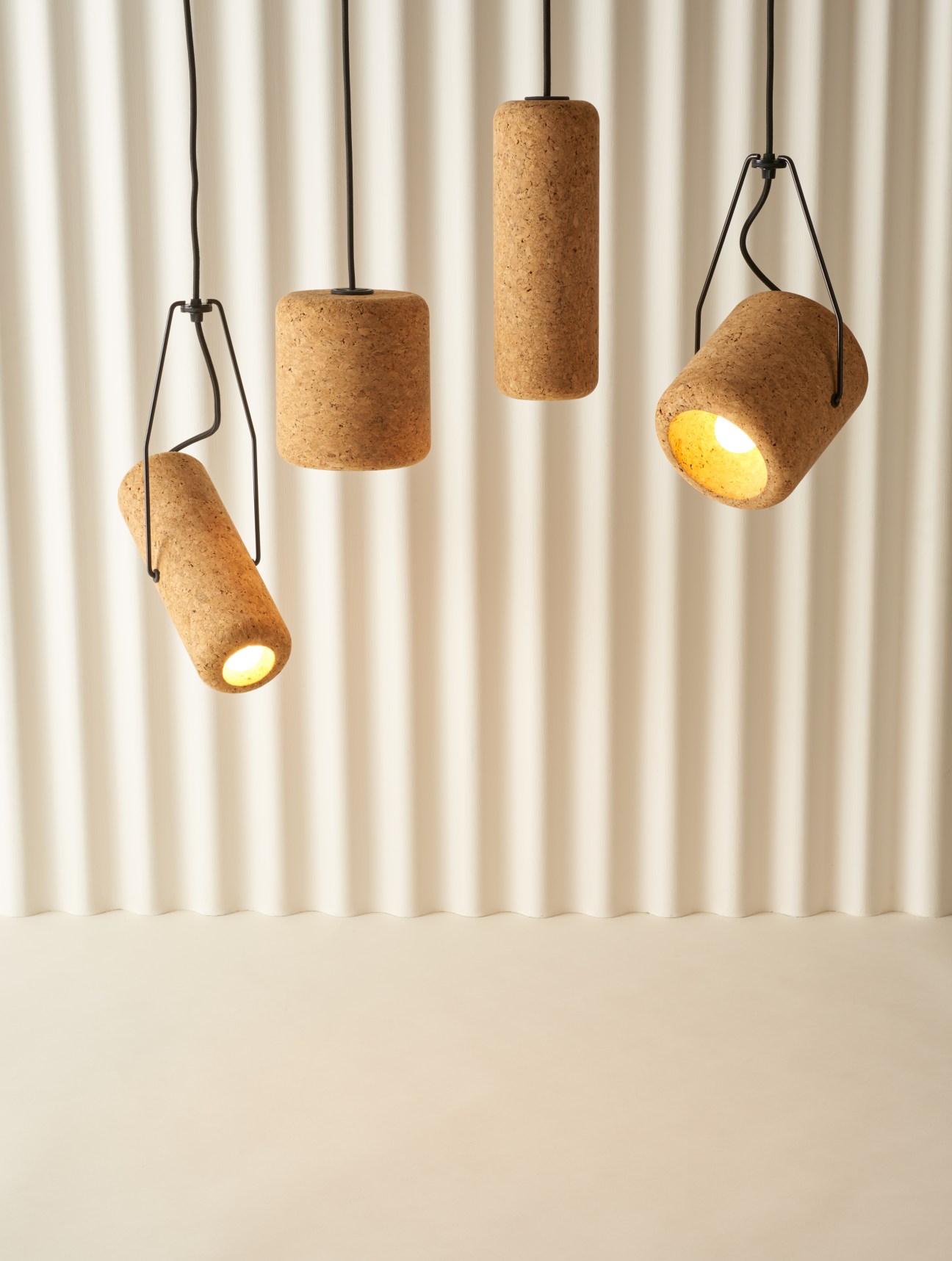 Four cork pendant lights by Max Harper in various cylindrical shapes suspended against a cream curtain backdrop.