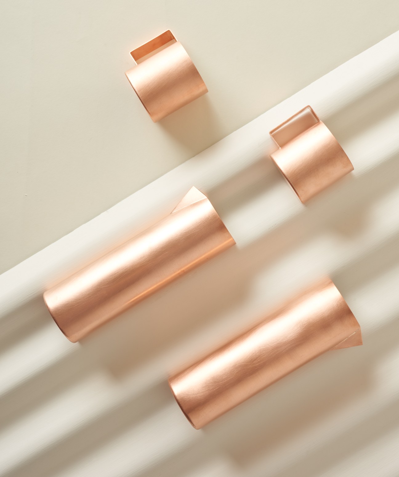 Copper mugs and pitchers by Studiokyss arranged on a white surface with shadows.