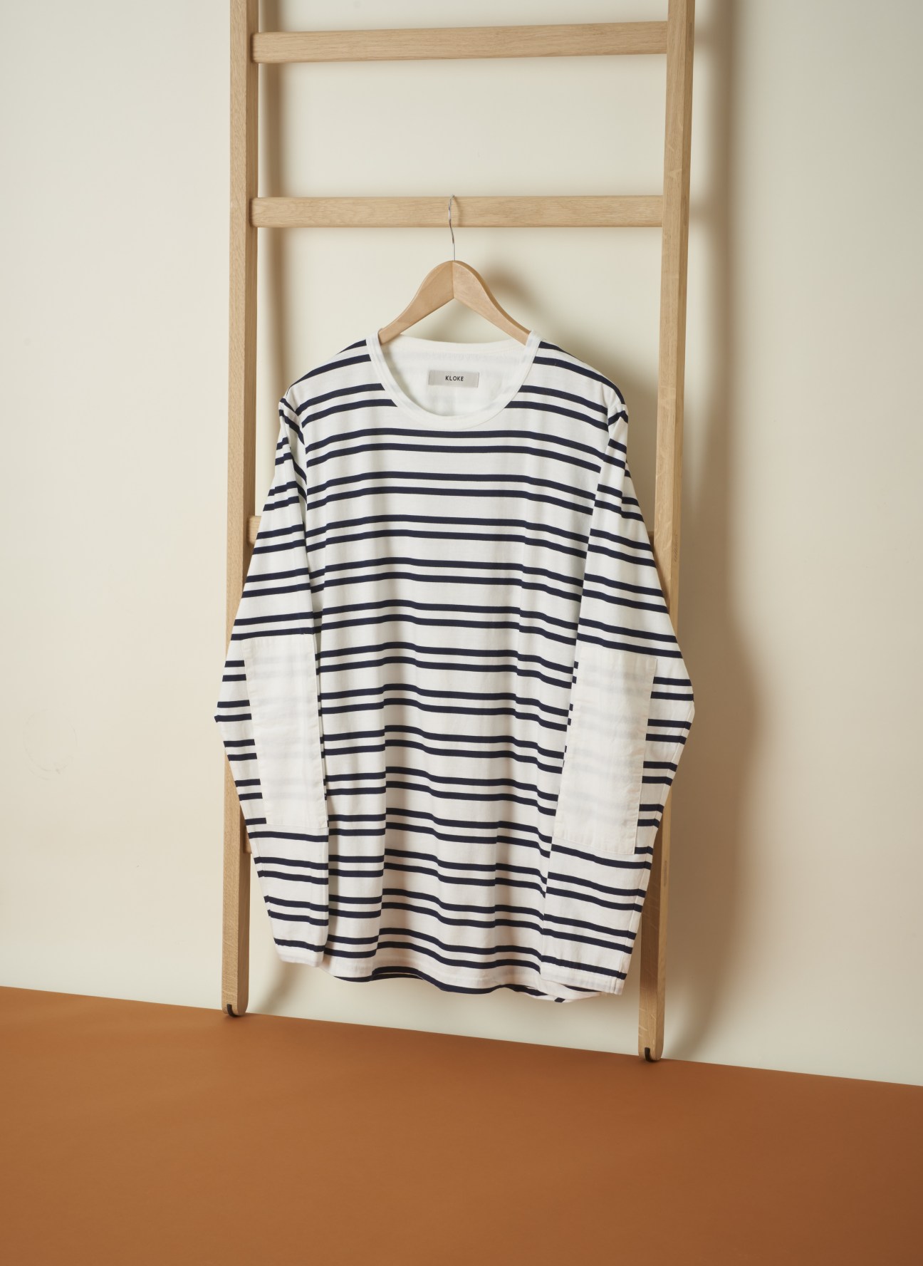 Kloke striped pullover with cotton elbow patches hanging on wooden ladder.