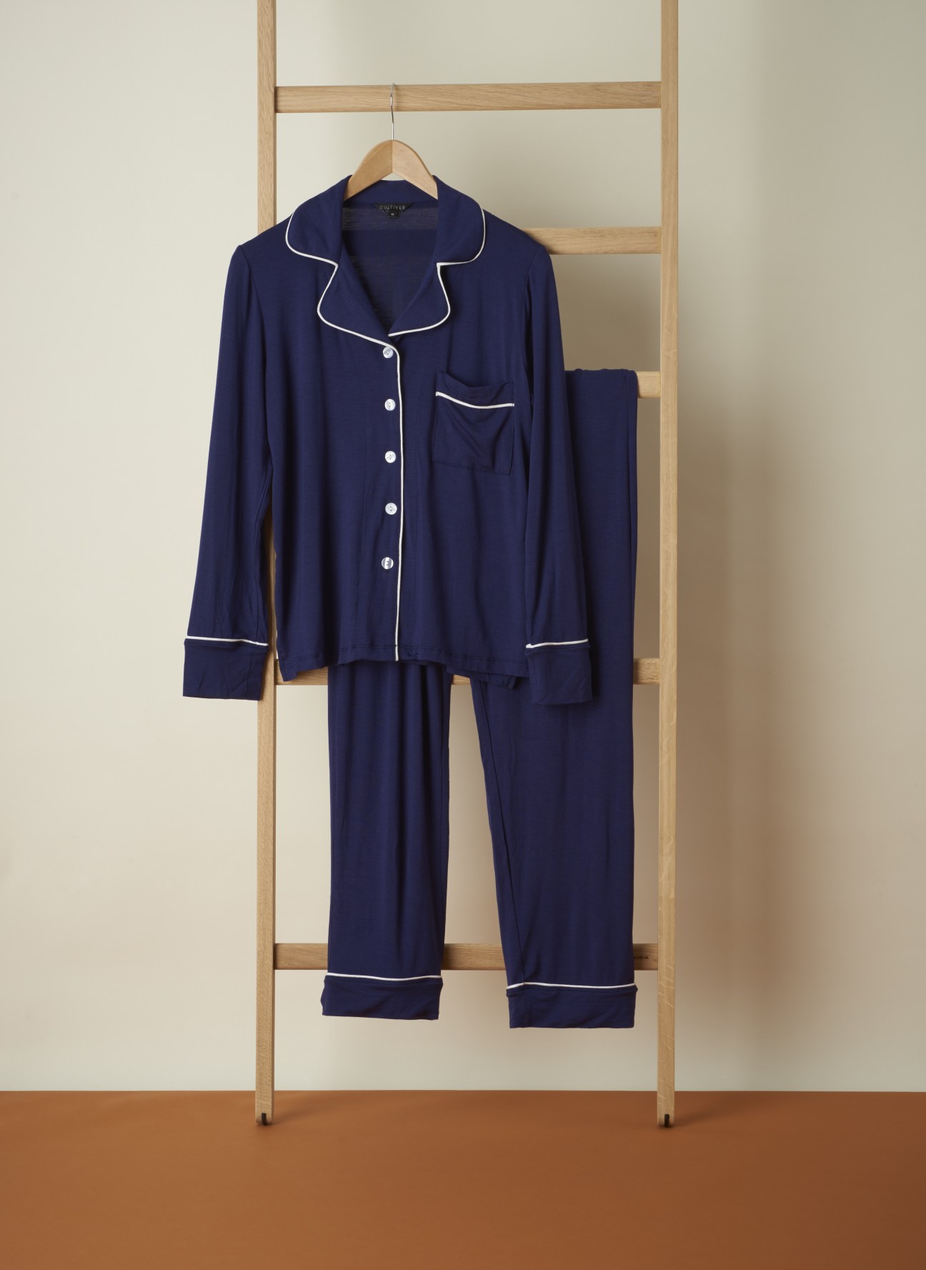 Navy pyjama set with white piping trim on wooden ladder rack.