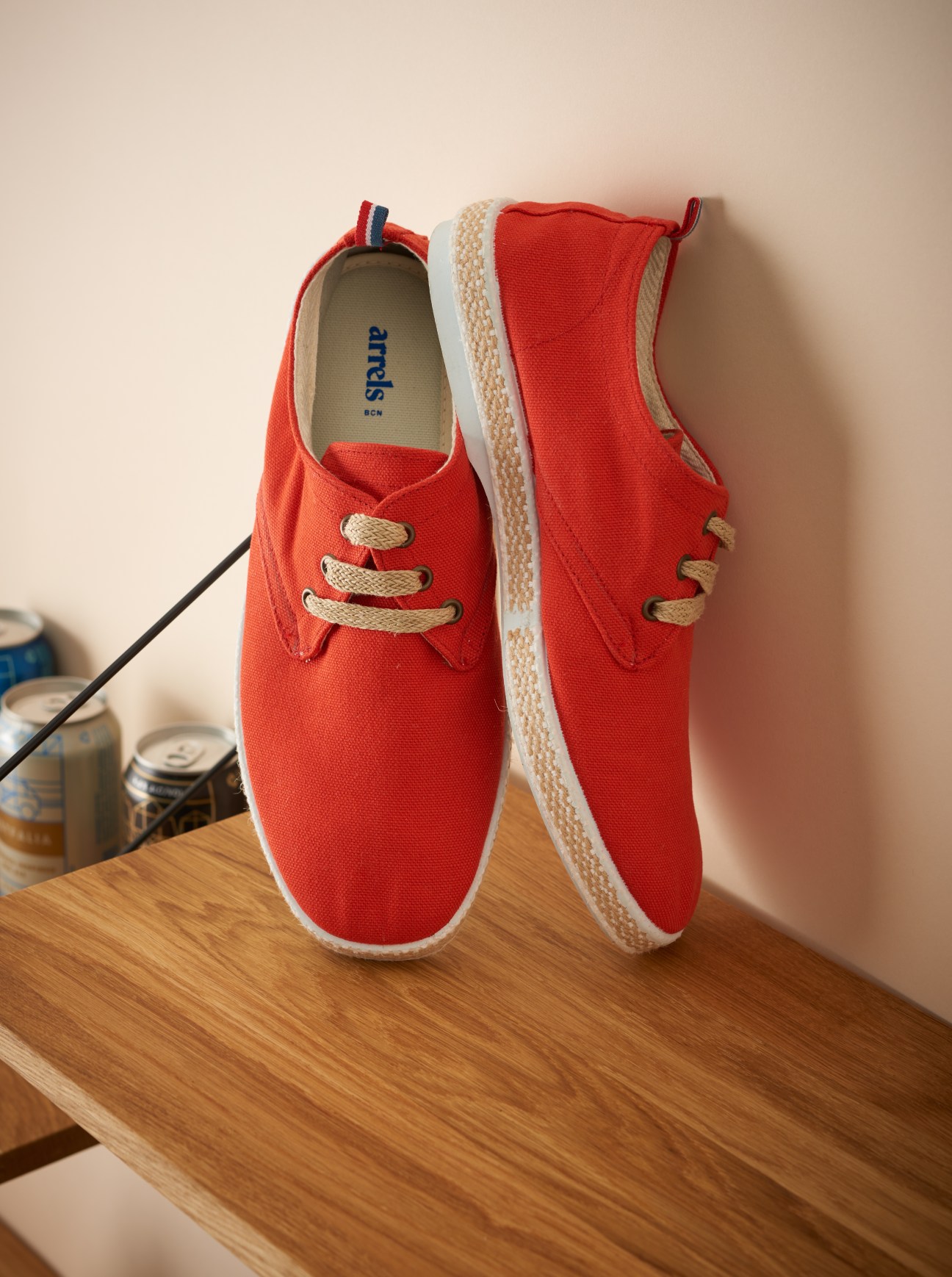 Red canvas Arrels shoes with white sole and tan laces displayed on wooden surface.