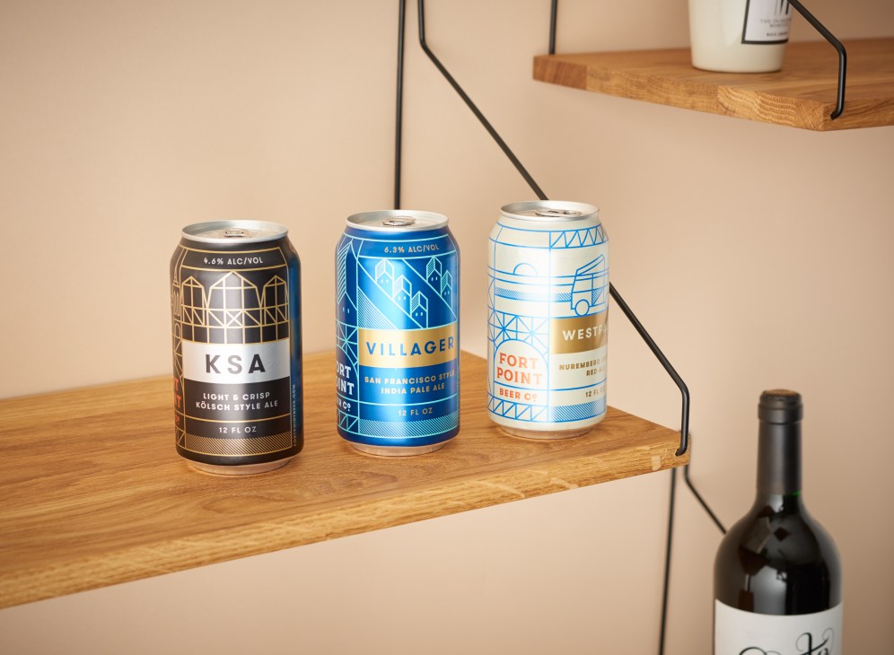 Three colorful beer cans displayed on a wooden shelf: KSA Kölsch-style ale, Villager San Francisco IPA, and Fort Point Brewery Nummemberg Red ale.