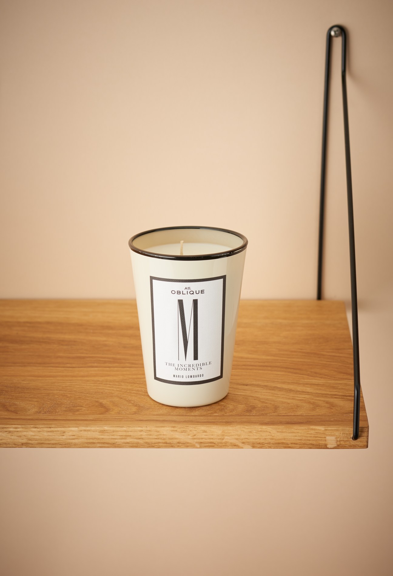 Atelier Oblique candle labeled 'M' from the Alphabet range on a wooden shelf with a black incense stick.
