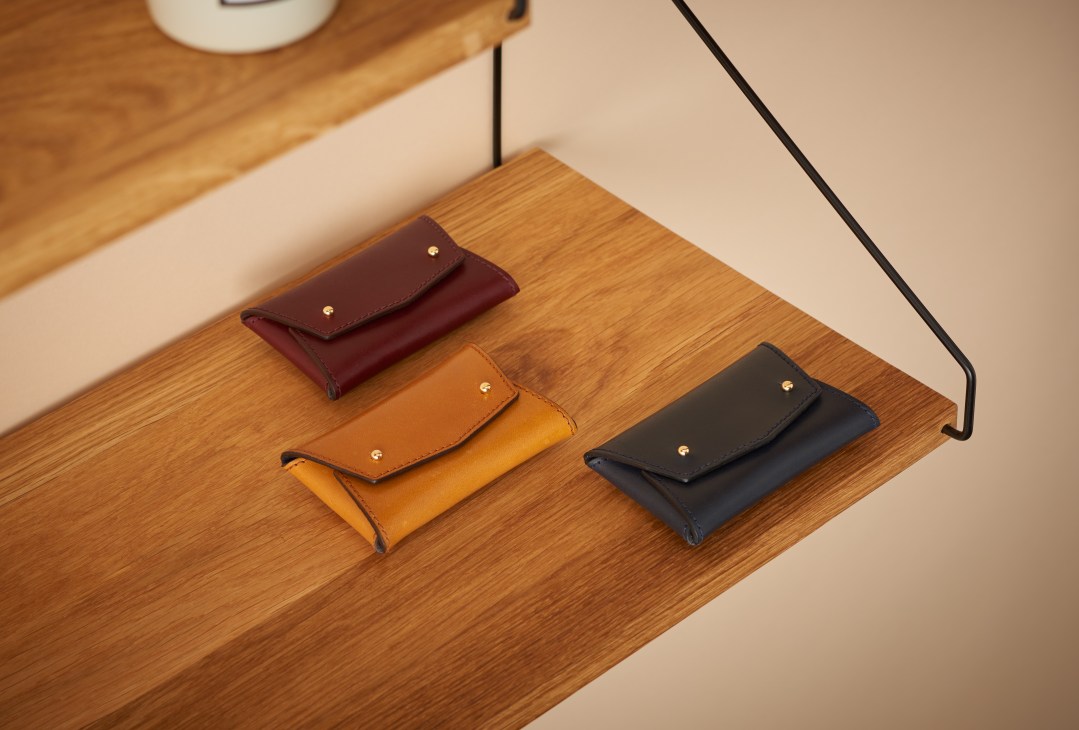 Three leather wallets by Stevan Saville in burgundy, tan and black displayed on a wooden surface.
