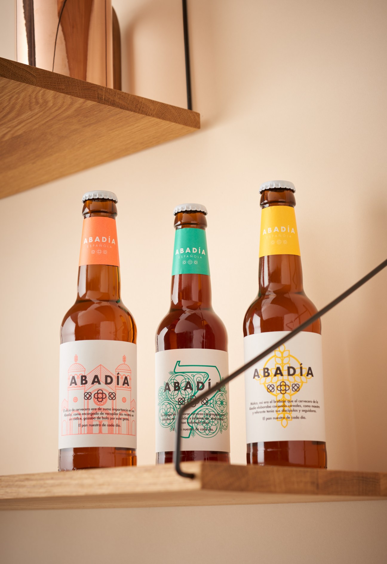 Three Abadía beer bottles with colorful labels displayed on a wooden surface.